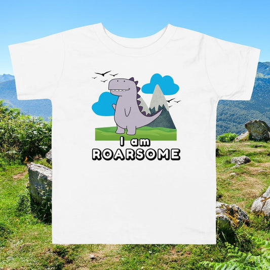 White toddler shirt with "I Am Roarsome" text and cartoon dinosaur in the center on a nature with greens and sky background—ideal for dino-loving kids.